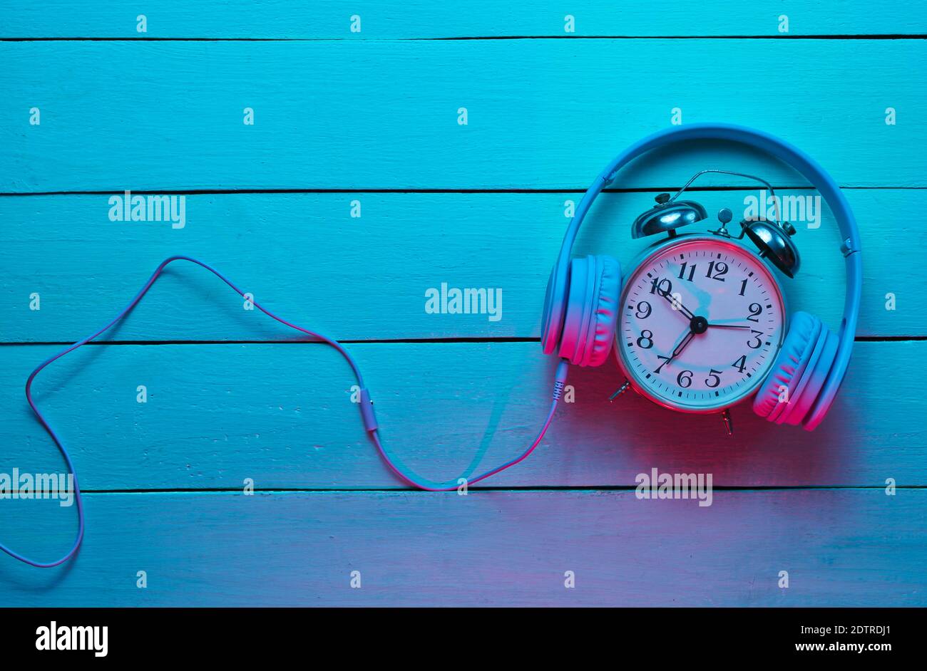 Vintage alarm clock with headphones on wooden background. Retro wave