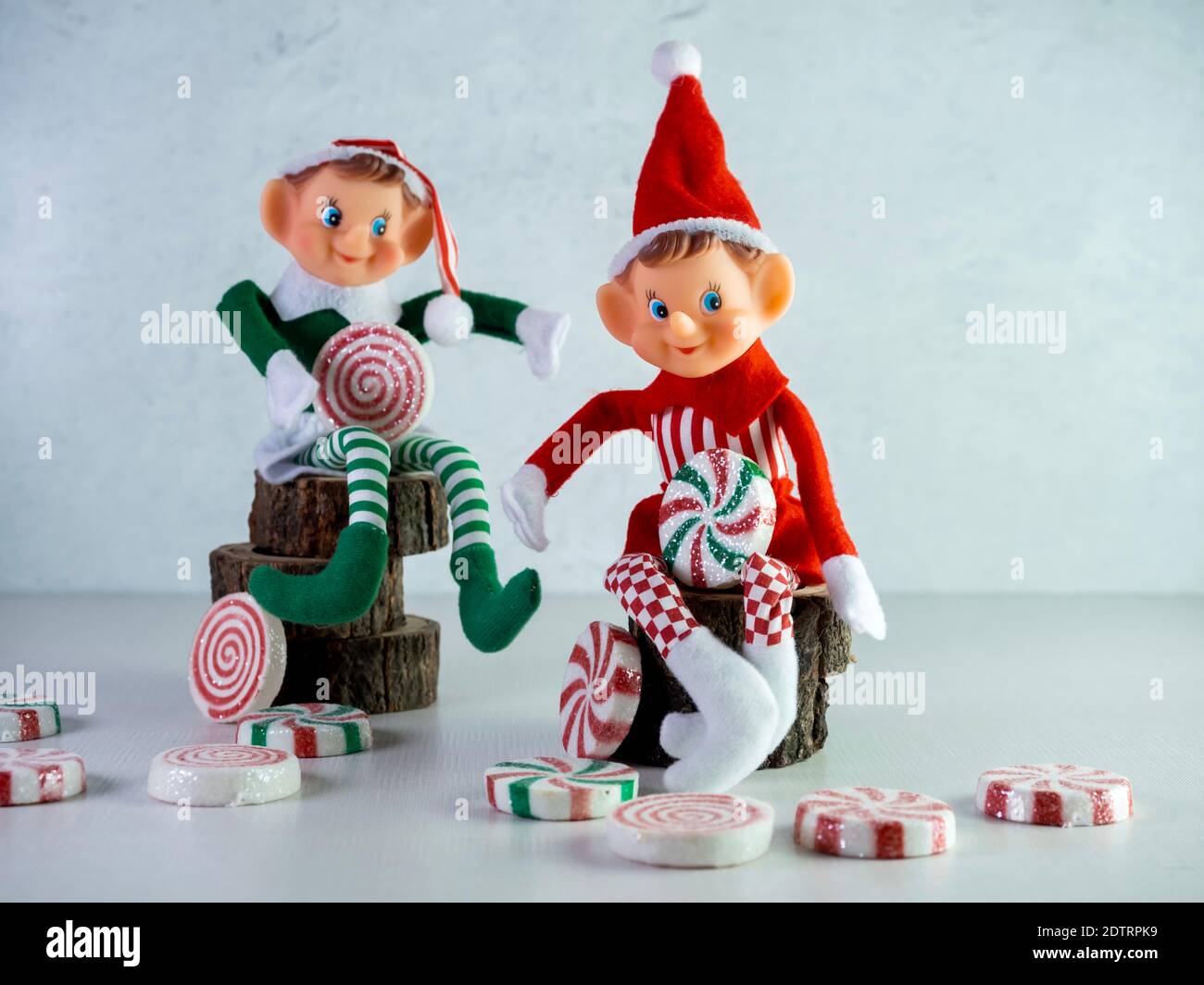Two Christmas Elves with Red and Green Outfits Sitting on Wood, holding large pieces of candy with more candy scattered around.  Holiday decor, Santa Stock Photo