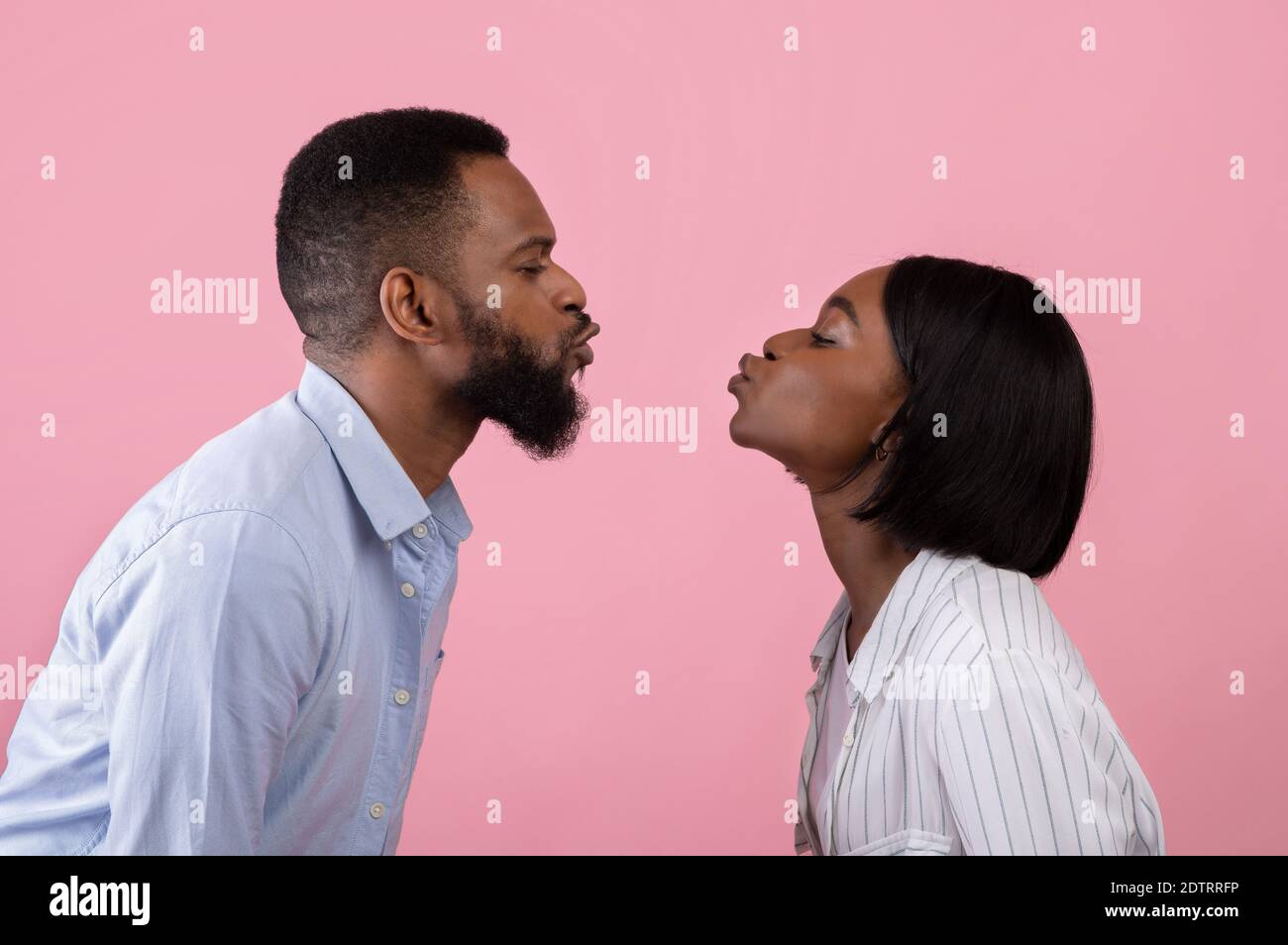 Young black couple in love pursing lips for kiss over pink studio background, side view. Celebrating romantic holiday Stock Photo