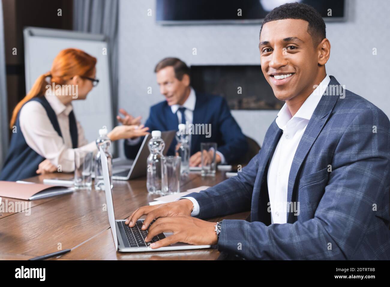 Happy african american businessman looking at camera while typing on ...