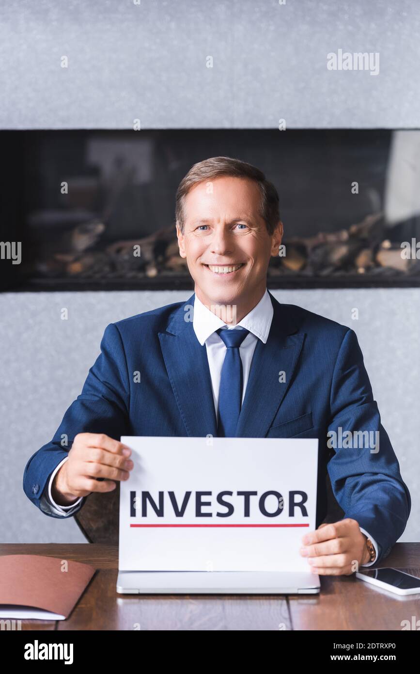 Smiling businessman looking at camera and holding sign with investor ...