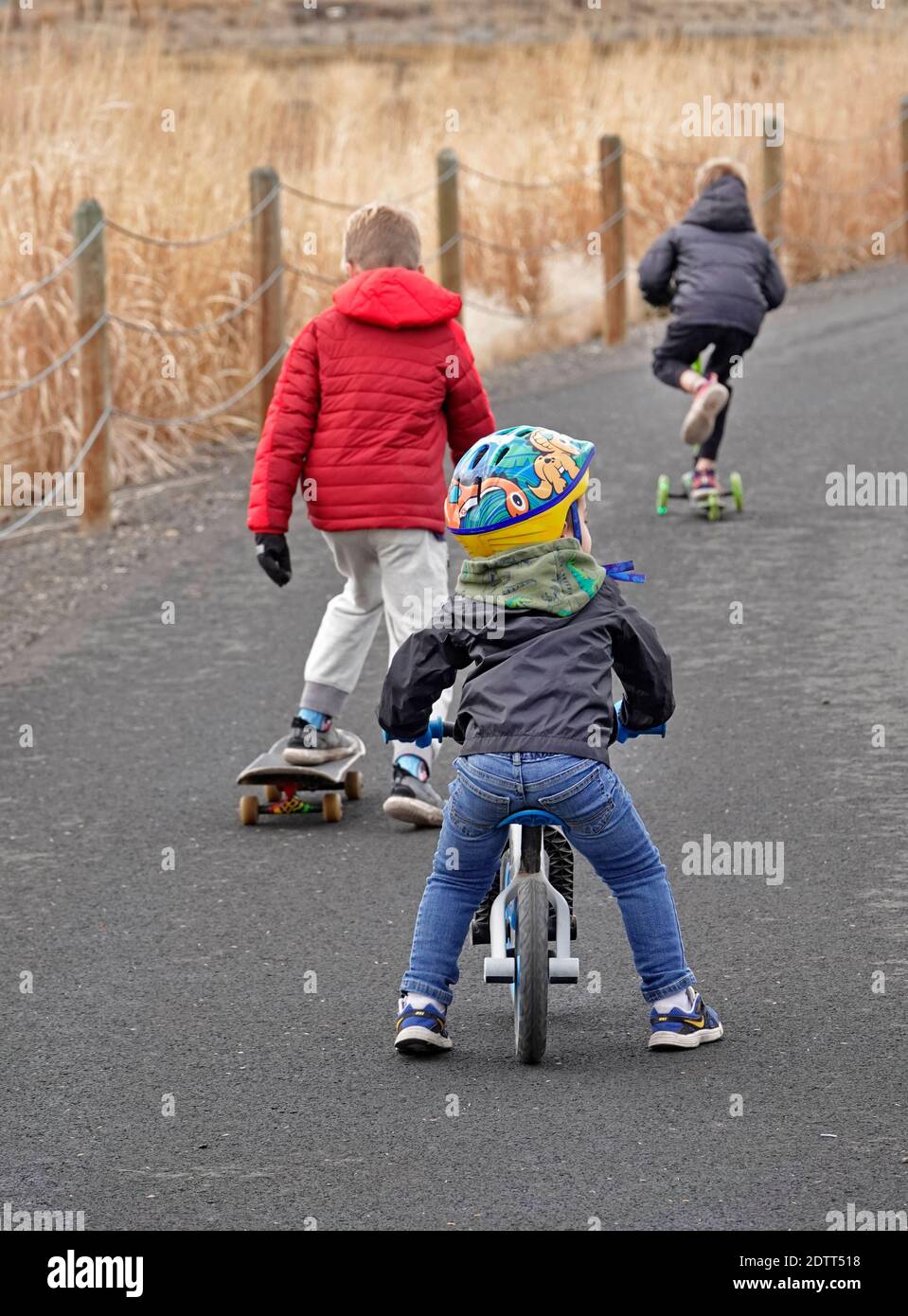Young children ride and skate and rollerboard along a paved pathway in an rural setting in central Oregon. Stock Photo