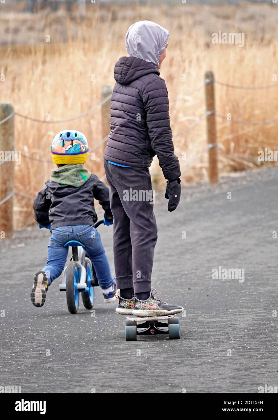 Young children ride and skate and rollerboard along a paved pathway in an rural setting in central Oregon. Stock Photo