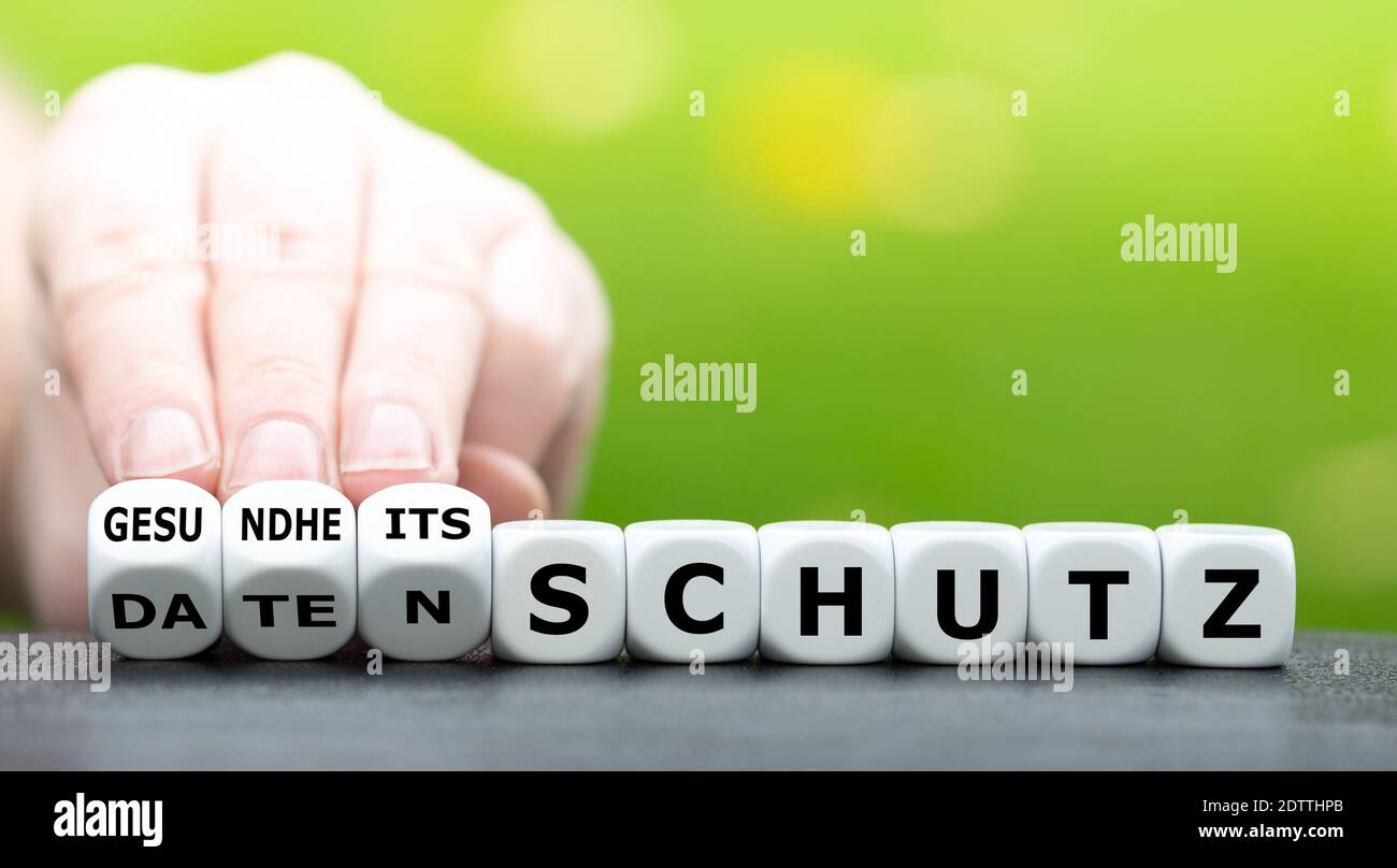 Data privacy vs health protection. Hand turns dice and changes the German expression 'Datenschutz' (data privacy) to 'Gesundheitsschutz' (health prote Stock Photo