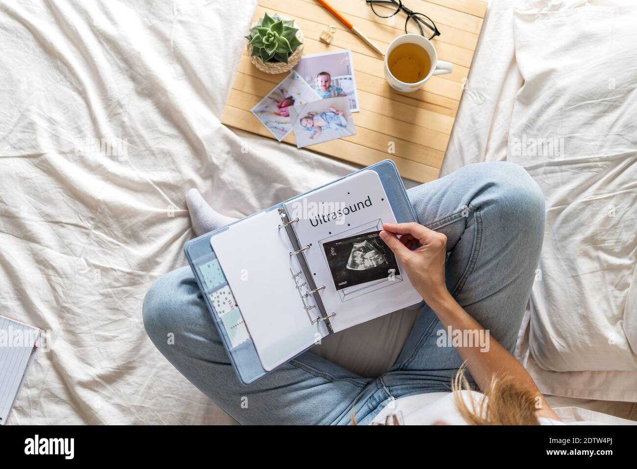 Cropped woman hands holding coffee and watching a family photo album. Mother sit on bed and watching album with little baby son kid boy Stock Photo