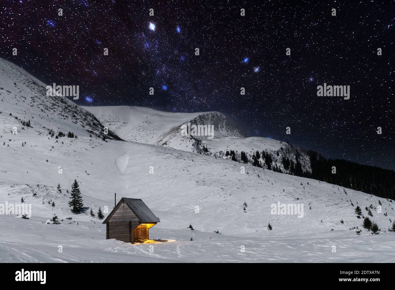 Fantastic winter landscape with wooden house in snowy mountains. Starry sky with Milky Way and snow covered hut. Christmas holiday and winter vacations concept Stock Photo