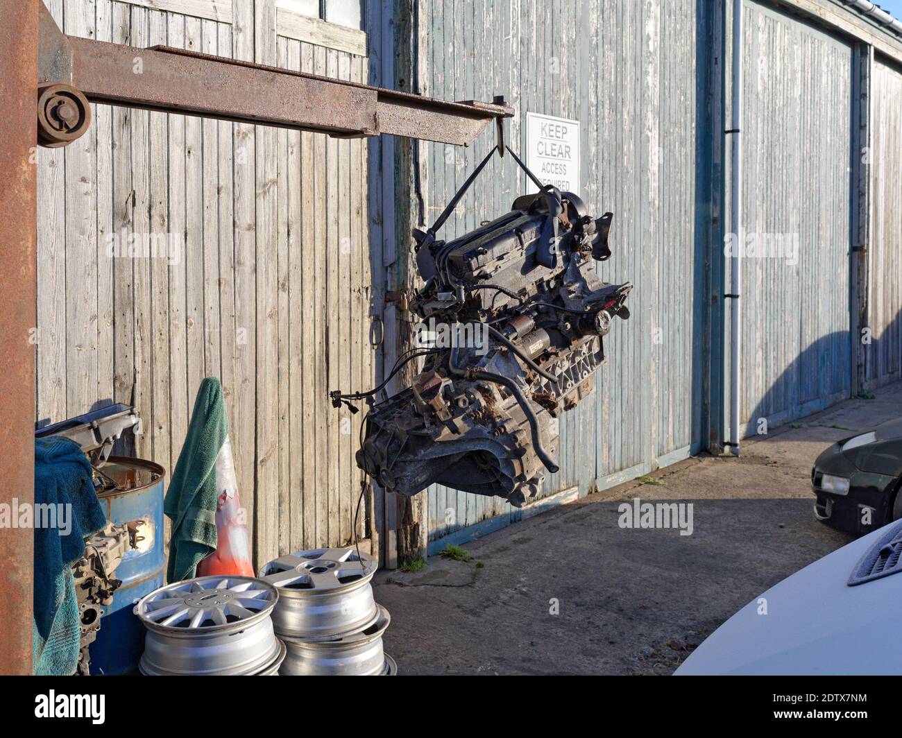 A car engine suspended in mid air on a crane outside a garage door Stock Photo