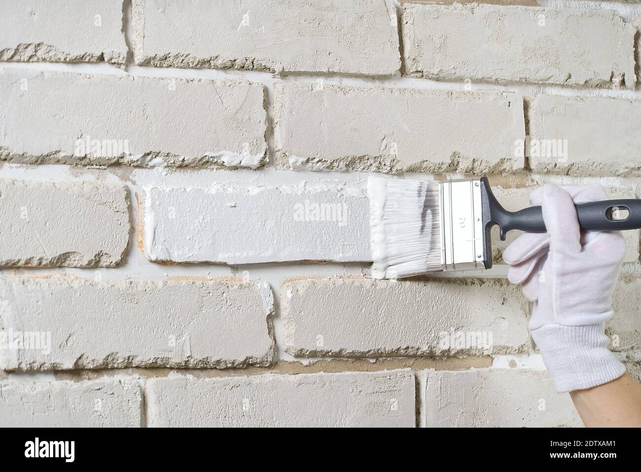 DIY wall repairing, Woman painting a white brick wall with a paint