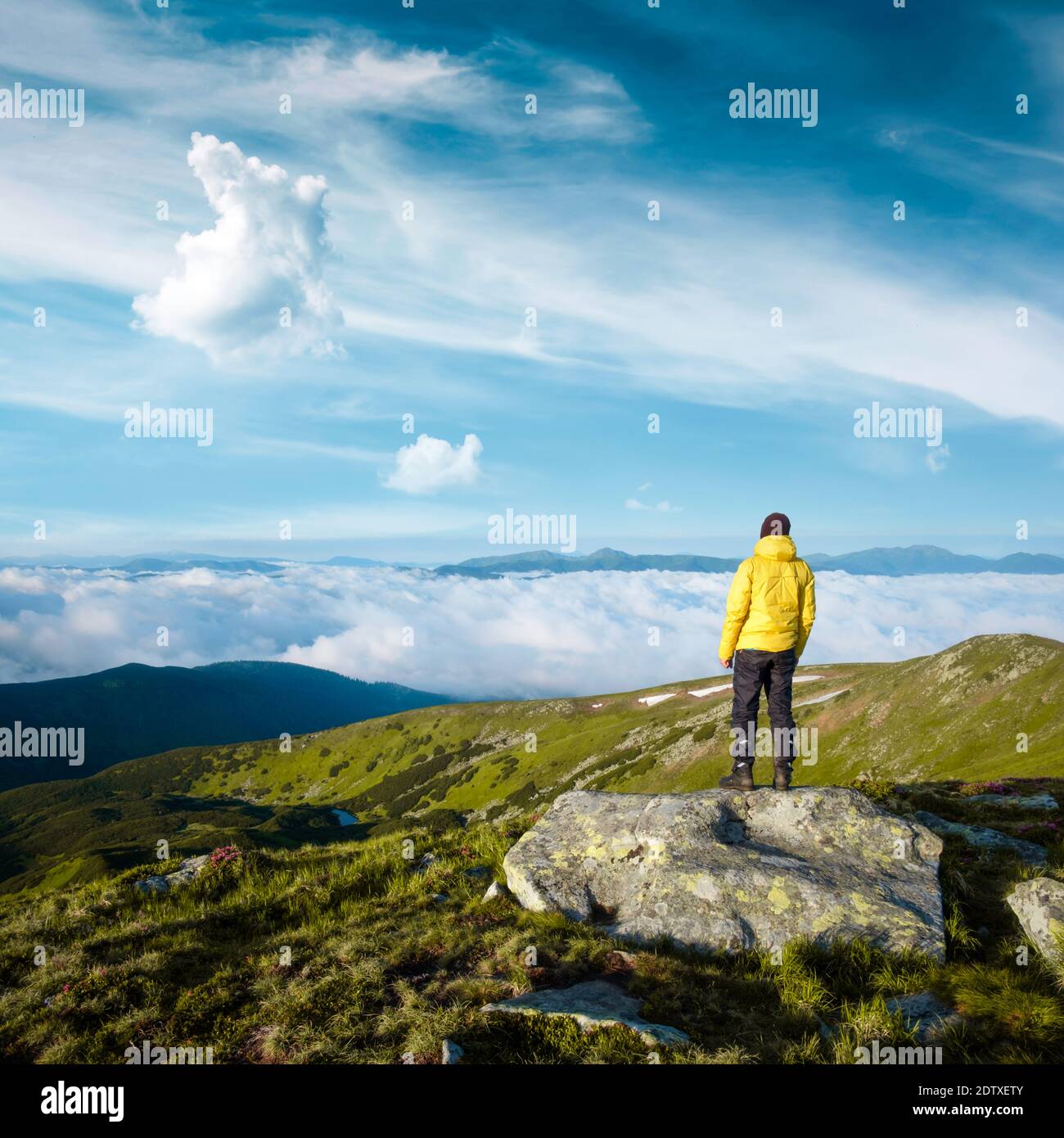 Alone tourist in yellow jacket stay on rock on high mountains. Landscape photography Stock Photo