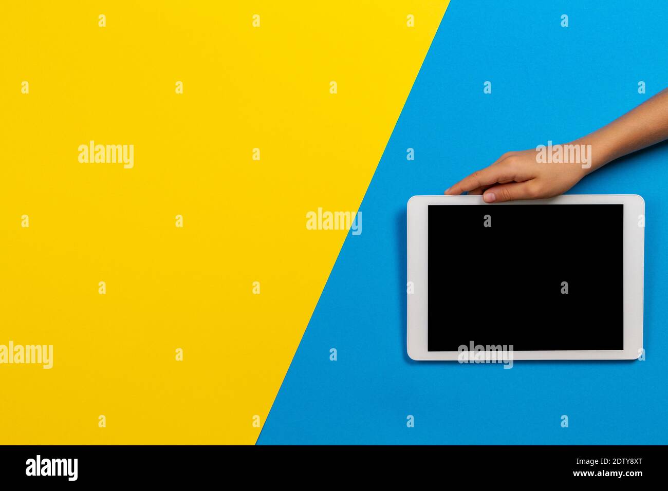 Kid hand holding digital tablet computer on yellow and light blue background Stock Photo