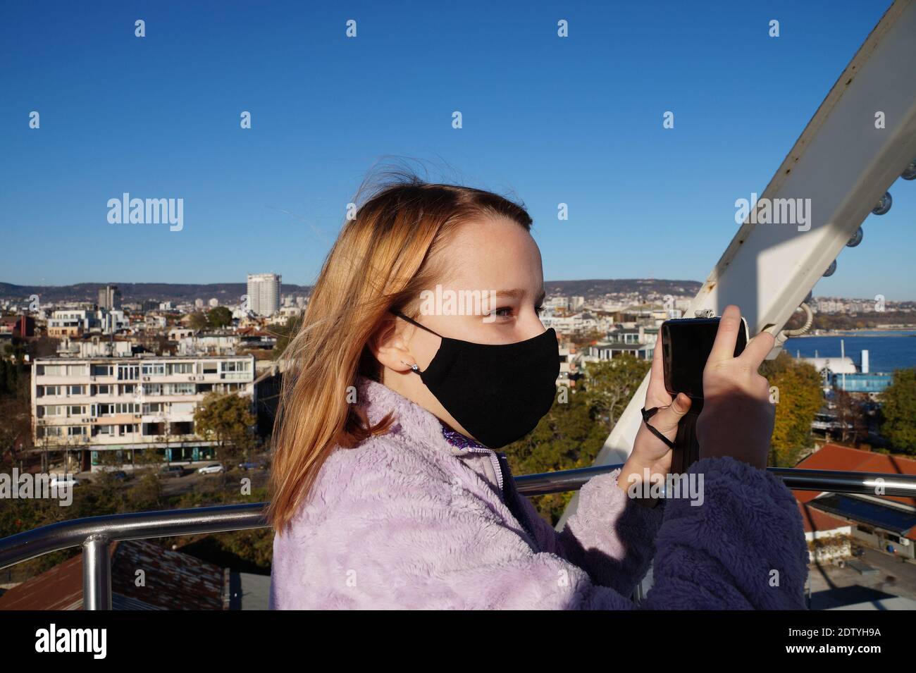 teenage girl in black medical mask takes selfie on ferris wheel. Stock Photo