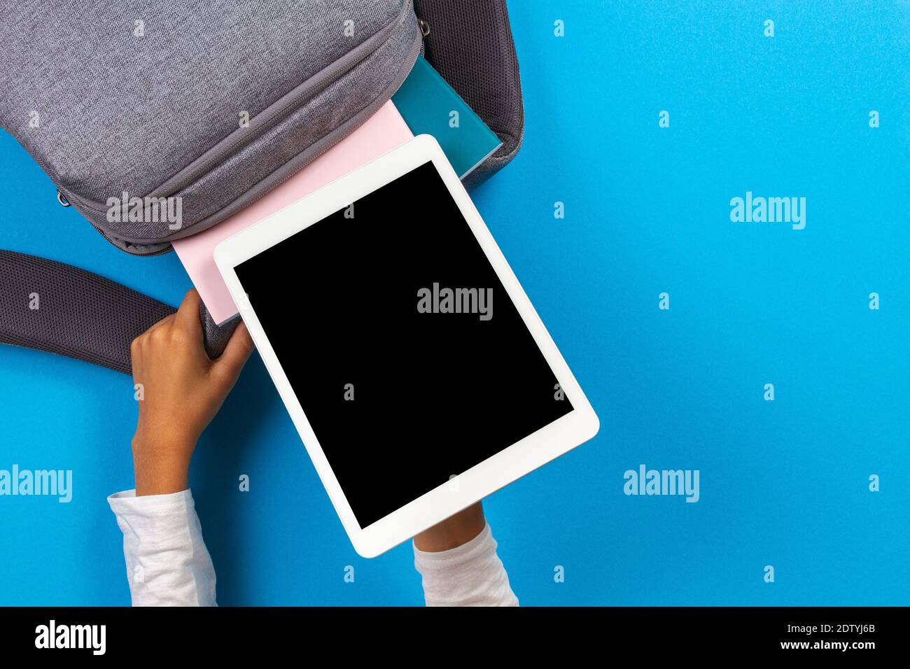 Kid hands taking digital tablet computer from gray backpack over light blue background. Top view Stock Photo