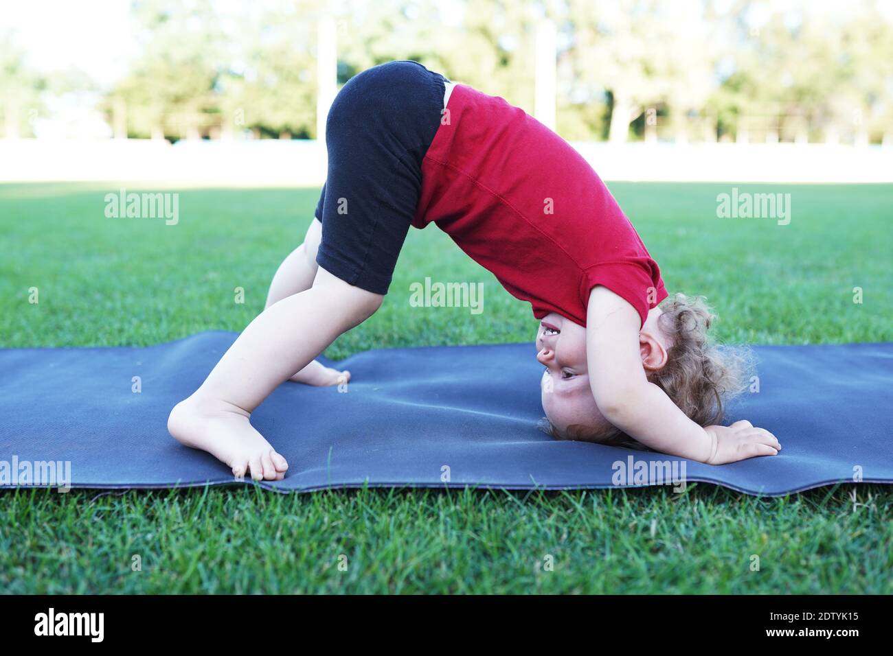Little cute baby girl doing yoga exercise on the grass at