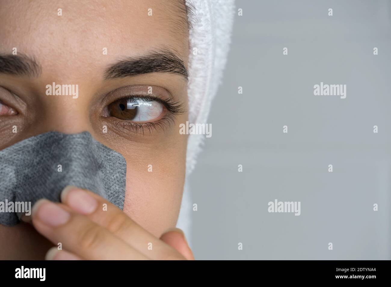 A woman sticks a cleansing strip on her nose. Black dots on the nose. Girl without makeup in the bathroom. Skin care, problem skin, cleansing. Natural Stock Photo