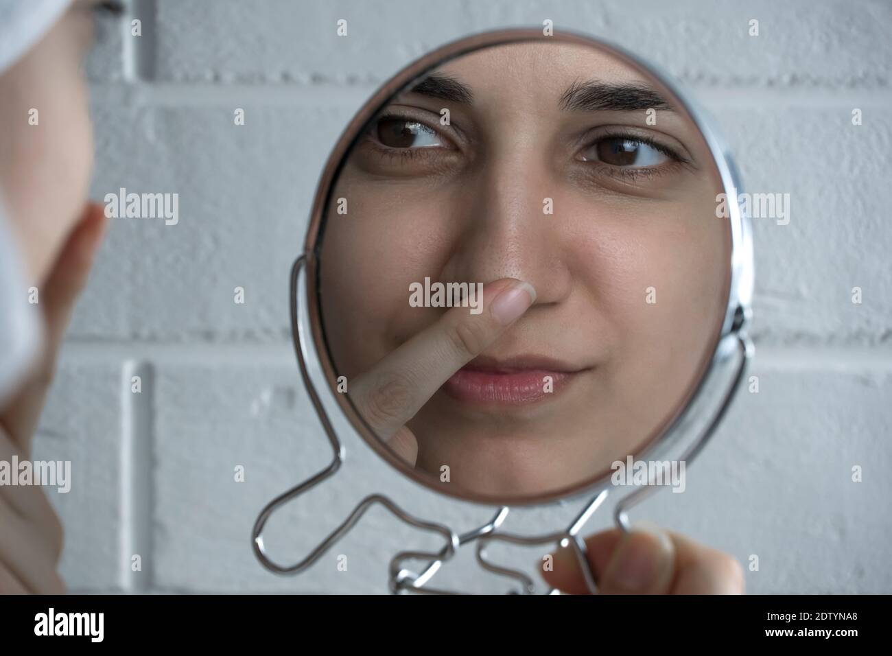 Black dots on the nose. A young woman looks at her face in the mirror. Skin care, problem skin, cleansing. Natural beauty, naturalness. Girl without m Stock Photo