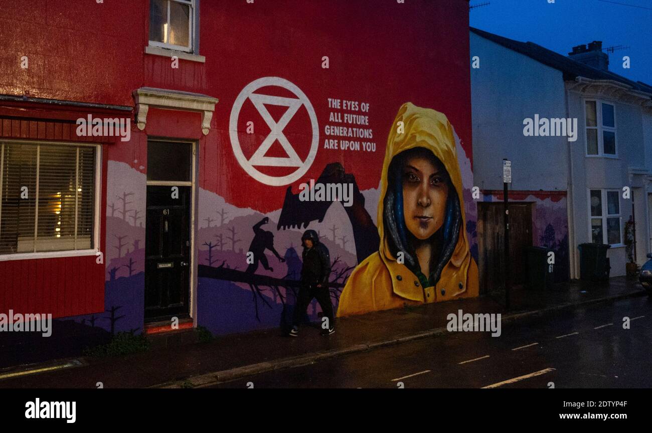 Brighton UK 22nd December 2020 - A man walks past a mural depicting Greta Thunberg and the Extinction Rebellion climate change protests in Brighton as heavy showers sweep across the South East this evening : Credit Simon Dack / Alamy Live News Stock Photo