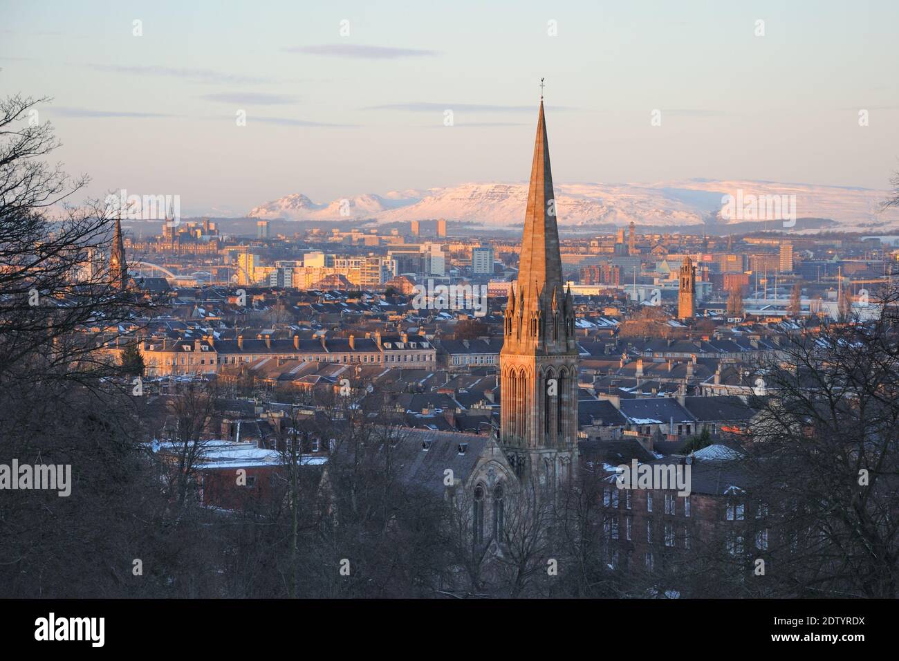 Evening sun skims the rooftops of Glasgow, Scotland, and illuminates the snow capped hills of the Campsie Fells to the north. Stock Photo