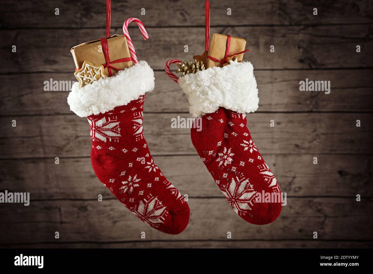 Pair of Christmas stockings filled with gifts and sweets hanging in front of a rustic wooden wall, selected focus Stock Photo