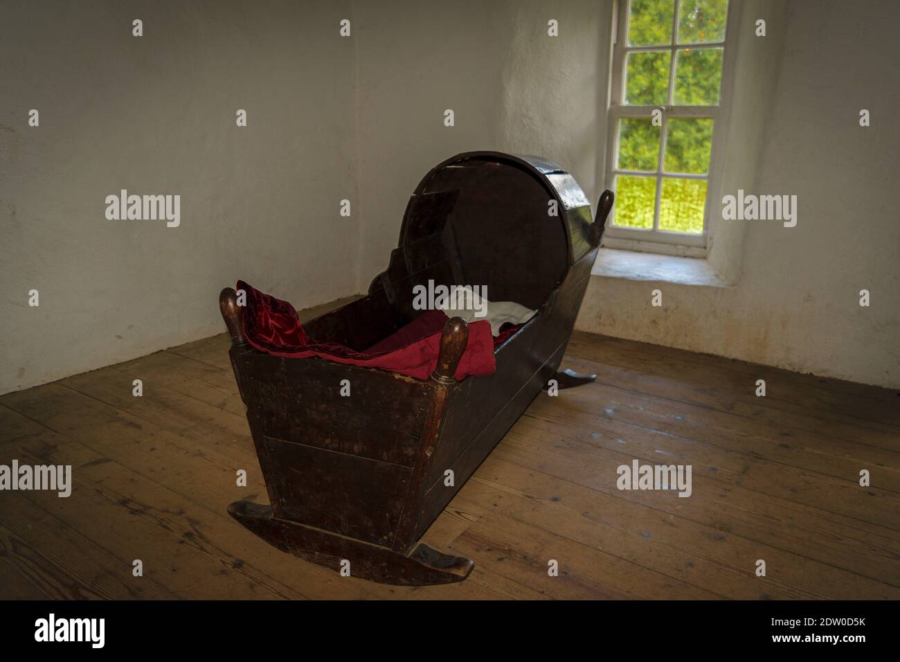 Wooden vintage antique rocking baby bed with the red blanket, in empty dark room with window and wooden floor Stock Photo