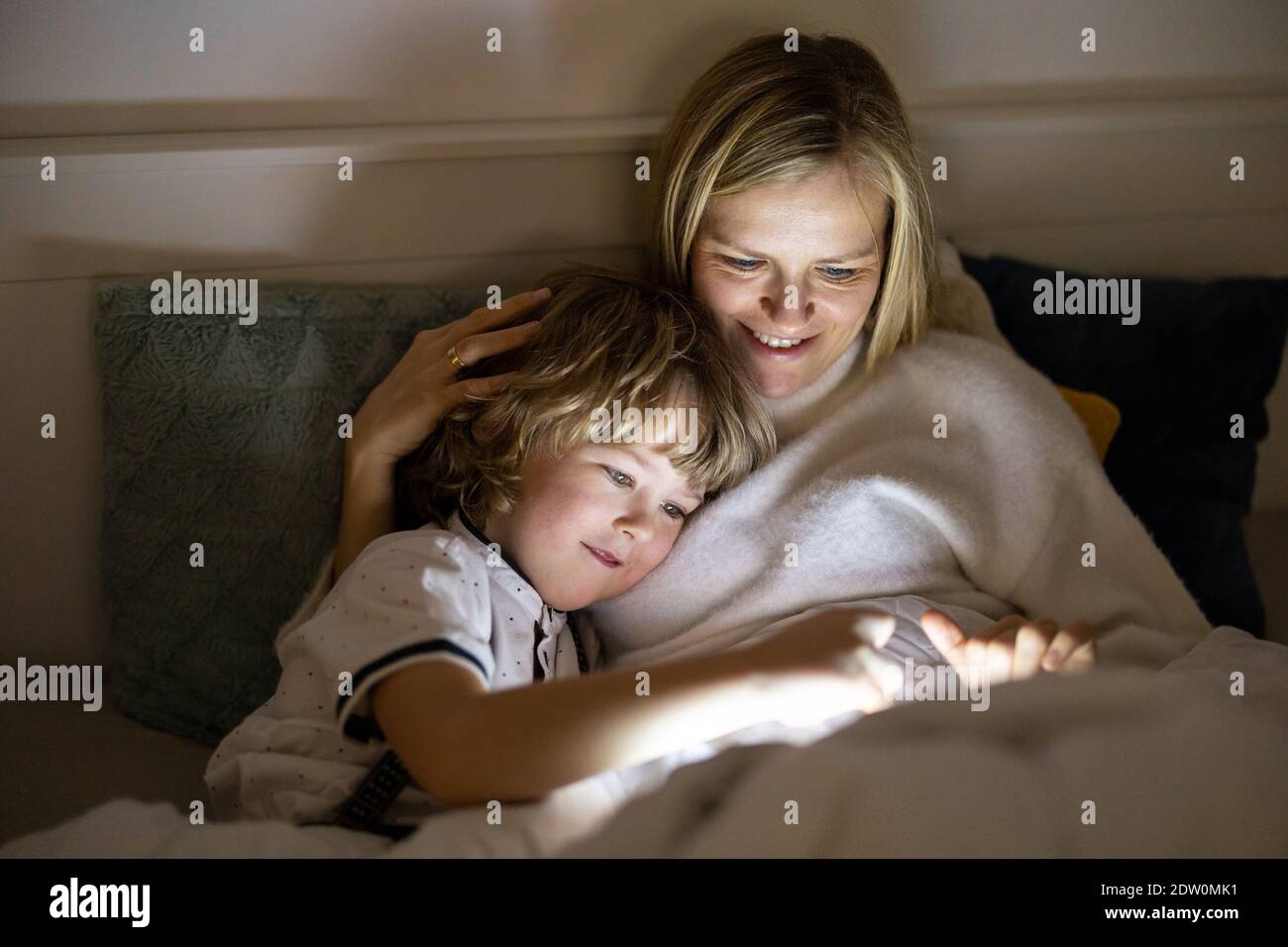 Mother and son using digital tablet together at night in bed Stock Photo