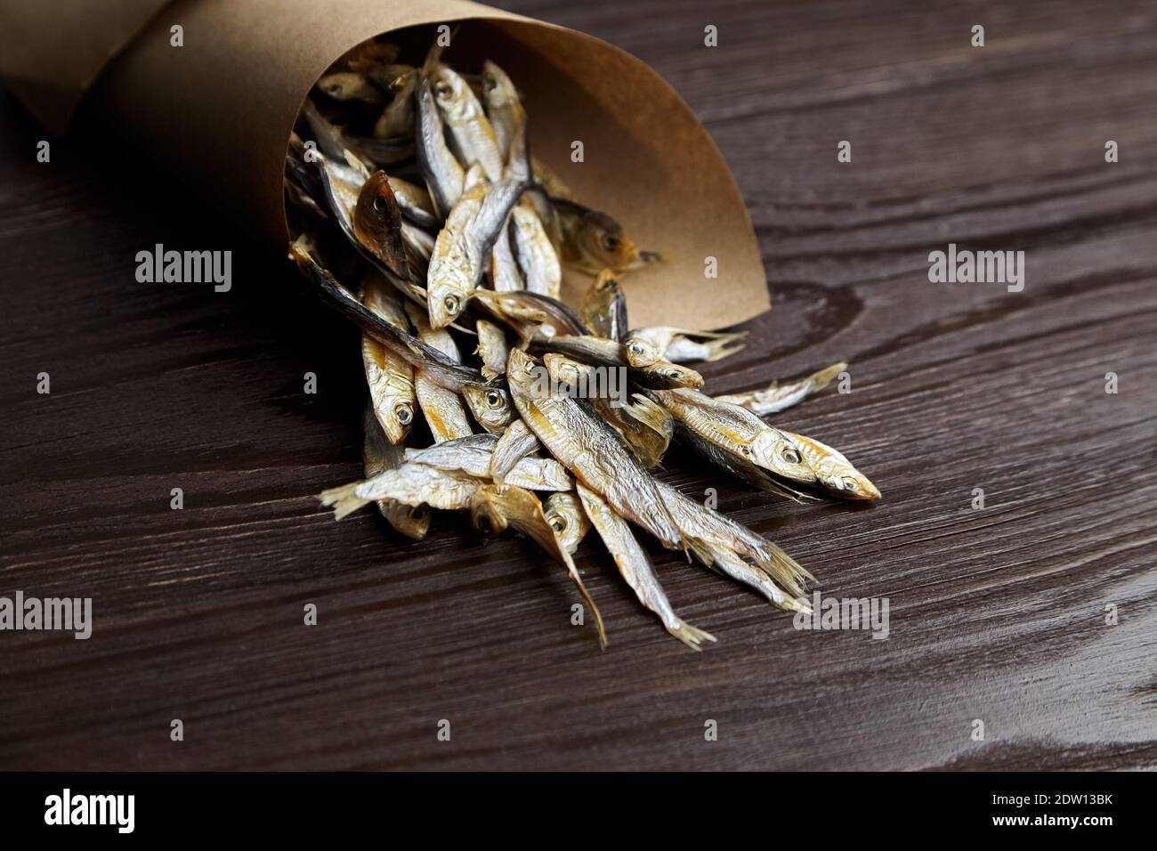 Sun-dried salty small fish. Stockfish in paper bag on dark wooden background. Stock Photo