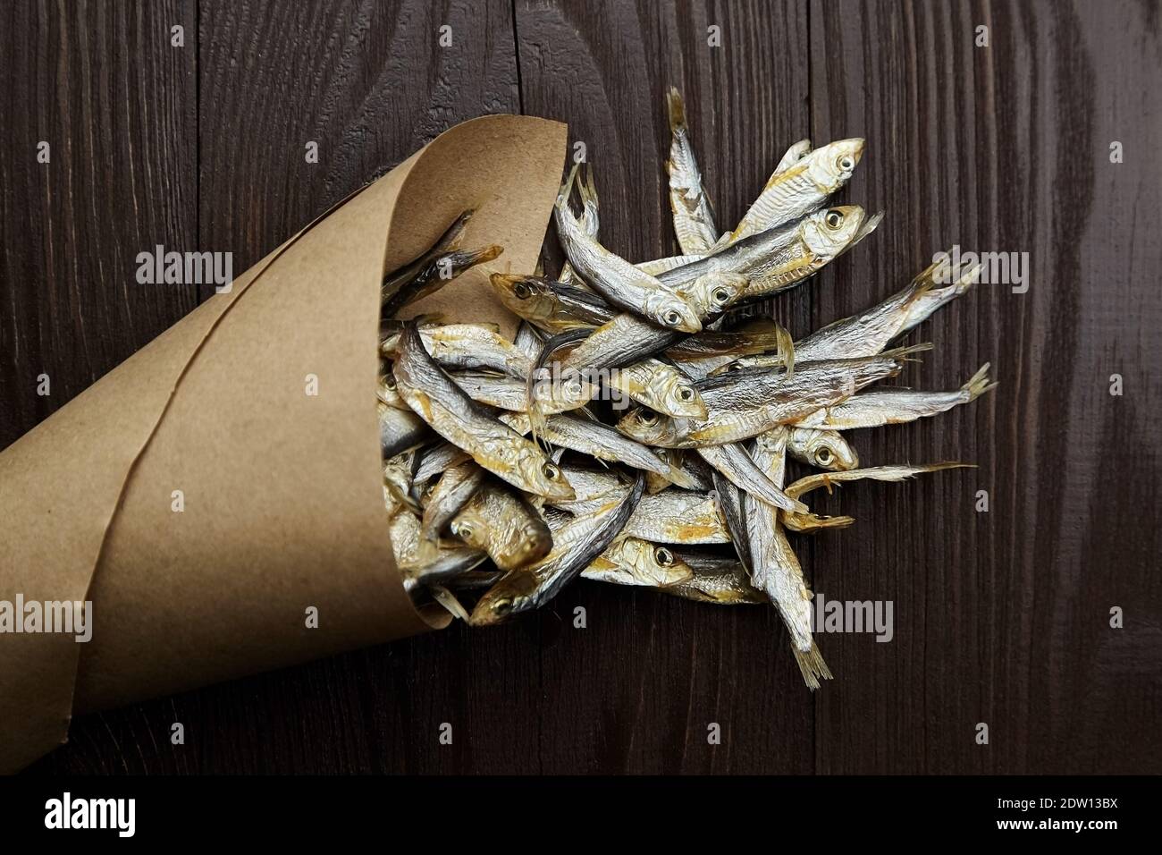 Sun-dried salty small fish. Stockfish in paper bag on dark wooden background. Stock Photo