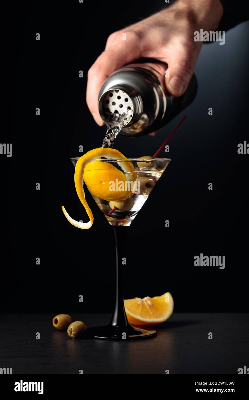 Bartender pour cocktail from shaker. Dry martini with lemon peel and