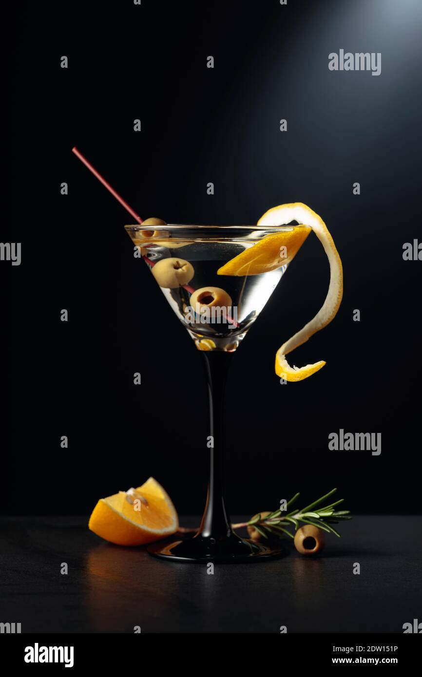 Dry martini with lemon peel and green olives on a black background
