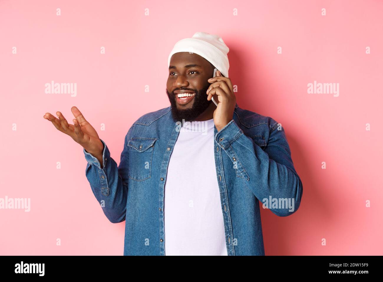 Handsome modern african-american man talking on mobile phone, smiling and discussing something, standing over pink background Stock Photo