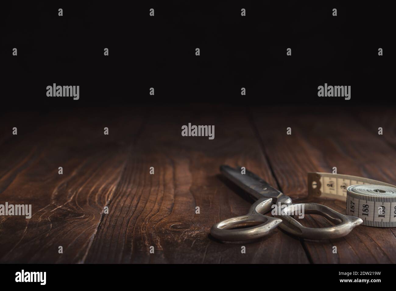 Sewing items - tailoring scissors and measuring tape on dark wooden table. Copy space for text. Stock Photo