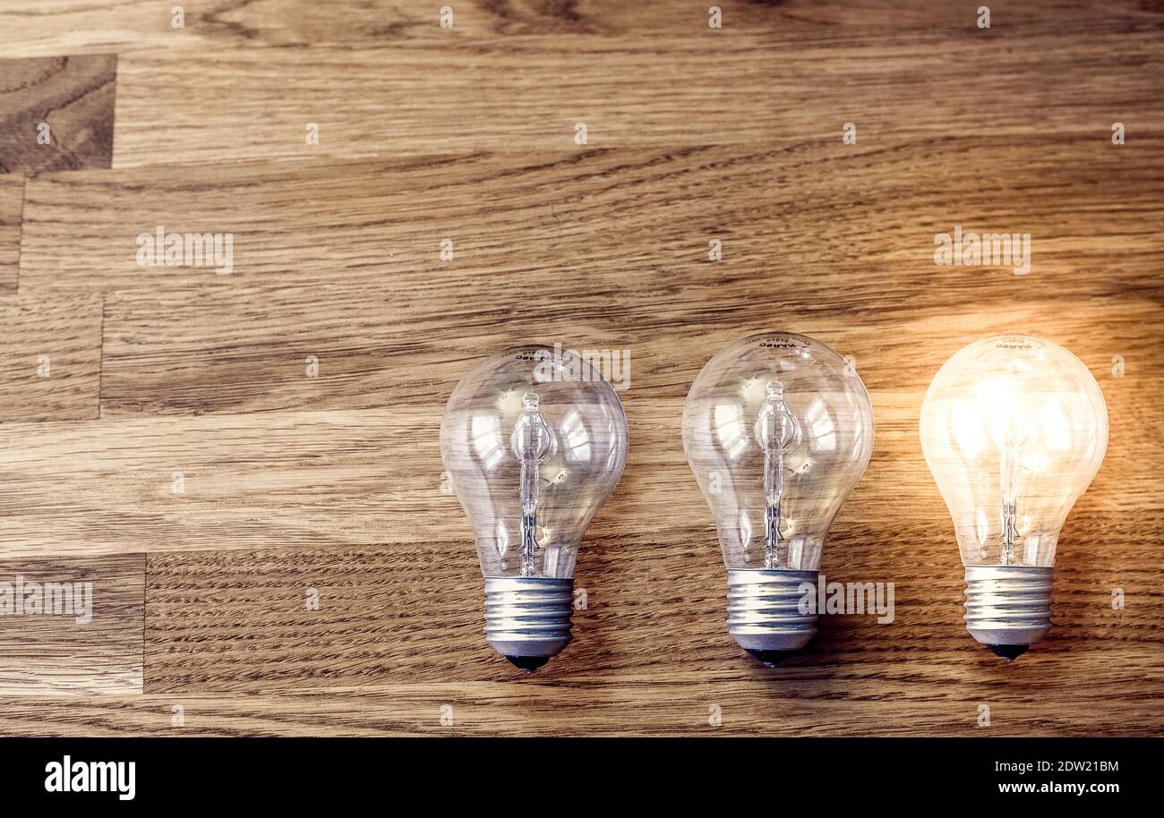 Three light bulbs on wooden table, one is lit. Concept for idea, thinking, problem solving Stock Photo