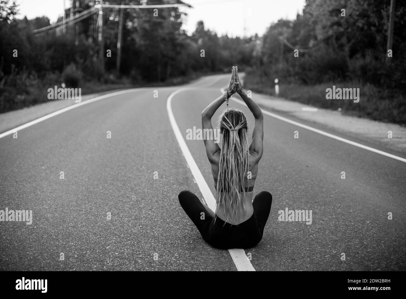 Yoga woman meditate sitting in the middle of the country road. Black ...