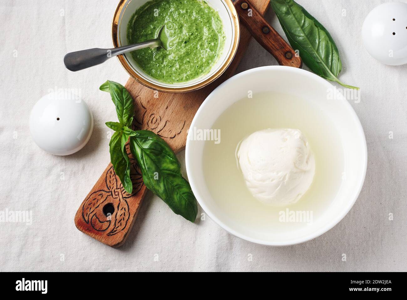 Mozzarella cheese ball in a bowl, pesto sauce and fresh basil leaves. Stock Photo