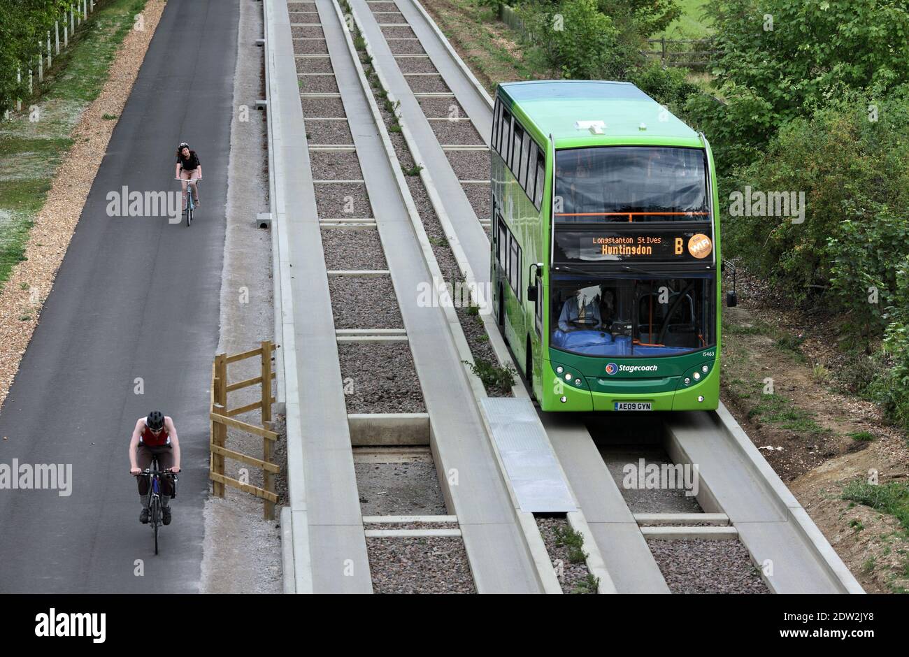 Cyclists on a cycle path are passed by a guided bus on the guided busway between Cambridge and St. Neots, Cambridgeshire. Stock Photo