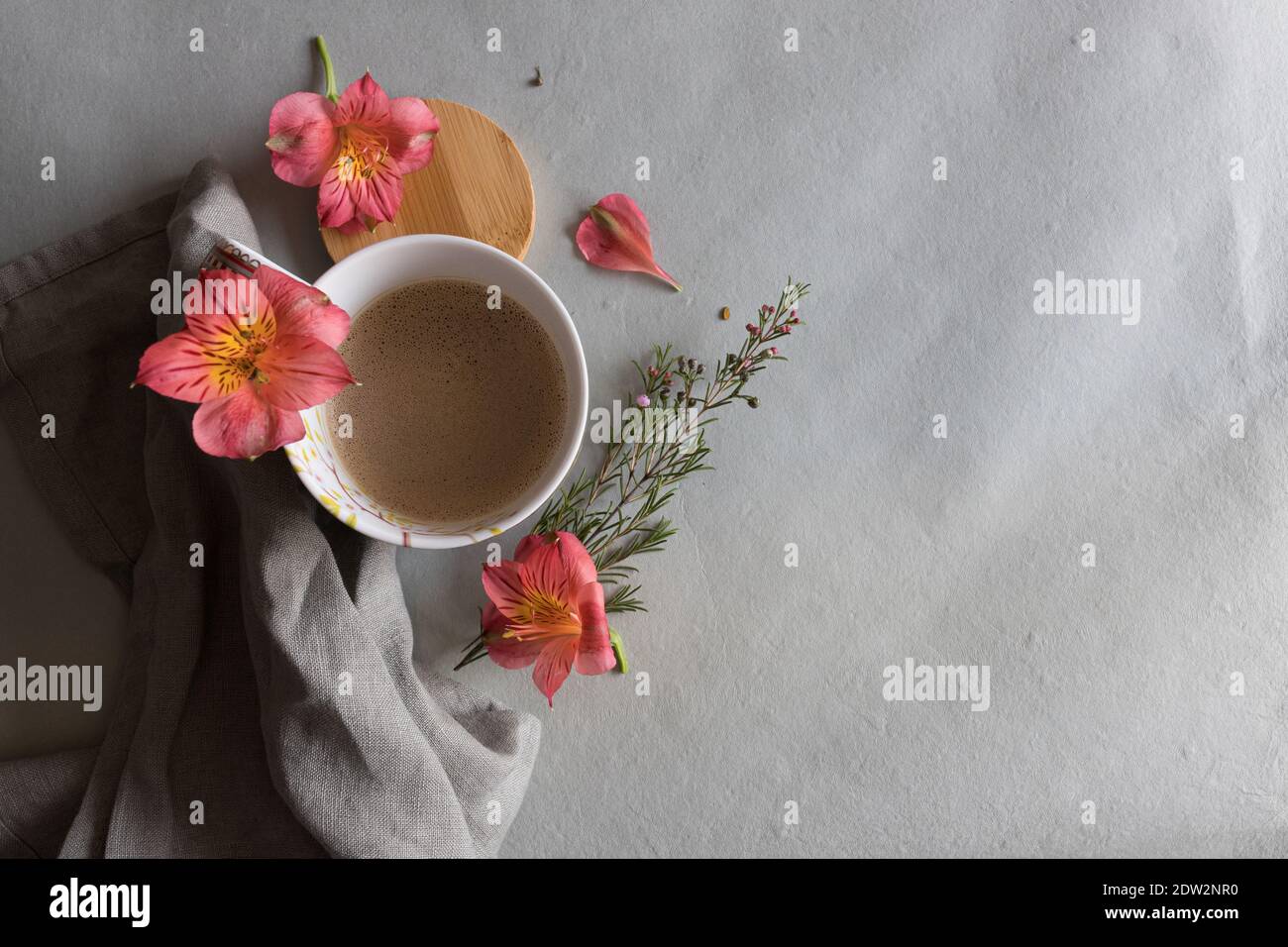 Overhead view of a cup of a foamy coffee with a beautiful red pink flower at the top and some additional flowers around it. Stock Photo
