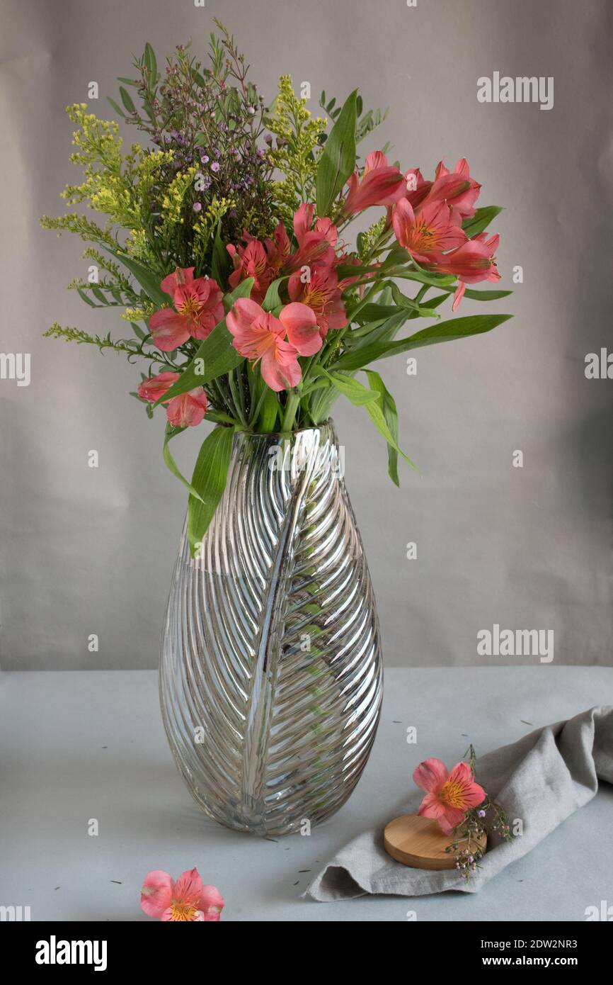 Closeup view of a beautiful crystal vase with a bouquet of red wild flowers inside. A wooden cover is over a rustic napkin next to it. Stock Photo