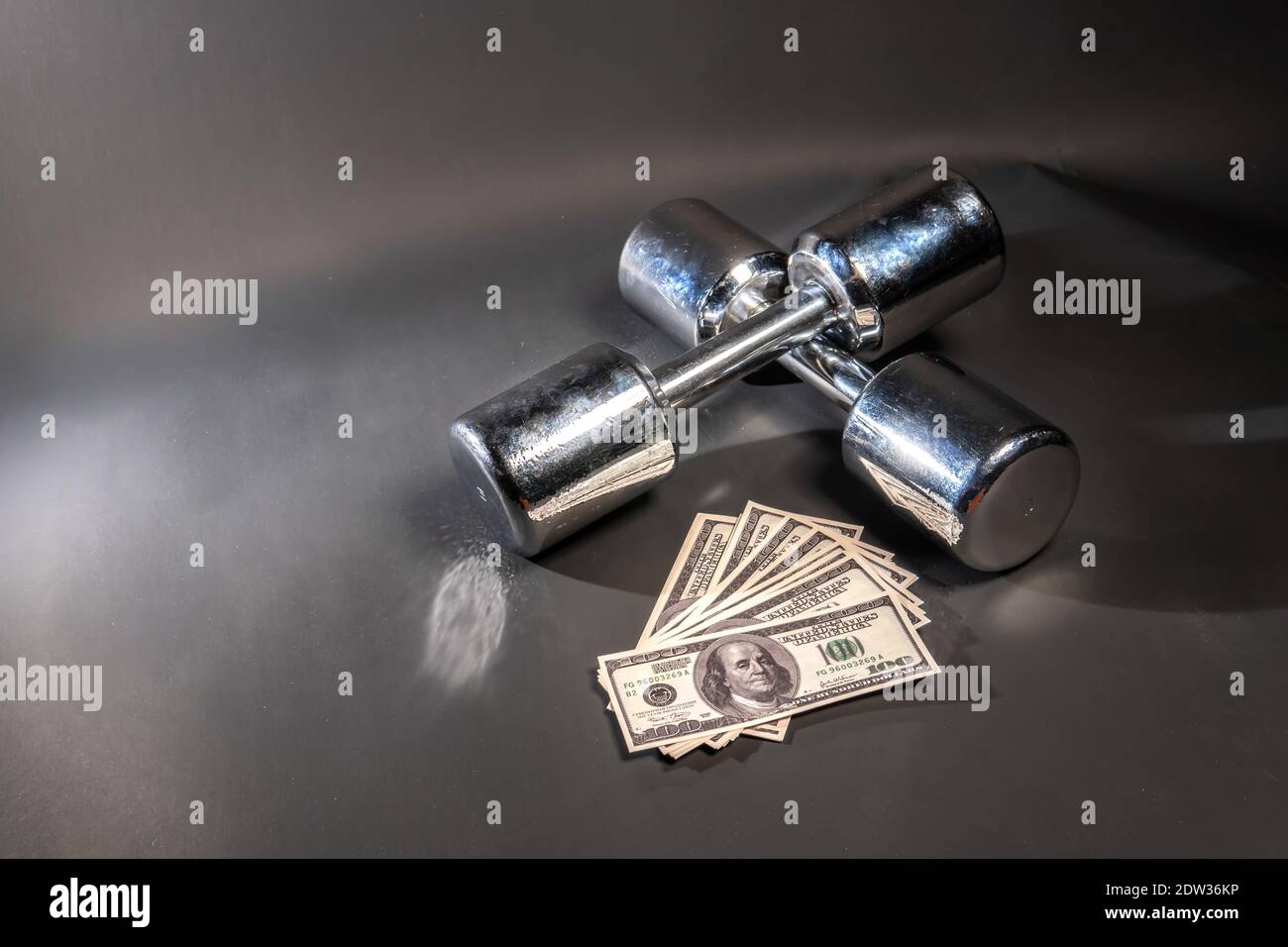 Bodybuilding dumbbells lie, money dollars glitter on a black background