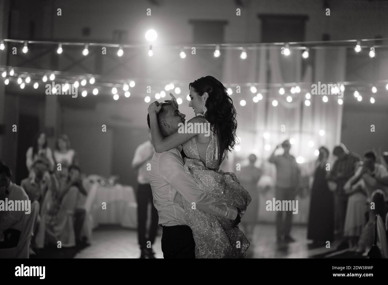 Groom holding the smiling bride in his hands. Happy newlyweds dancing at the wedding party. Newlyweds first dance. Black and white Stock Photo