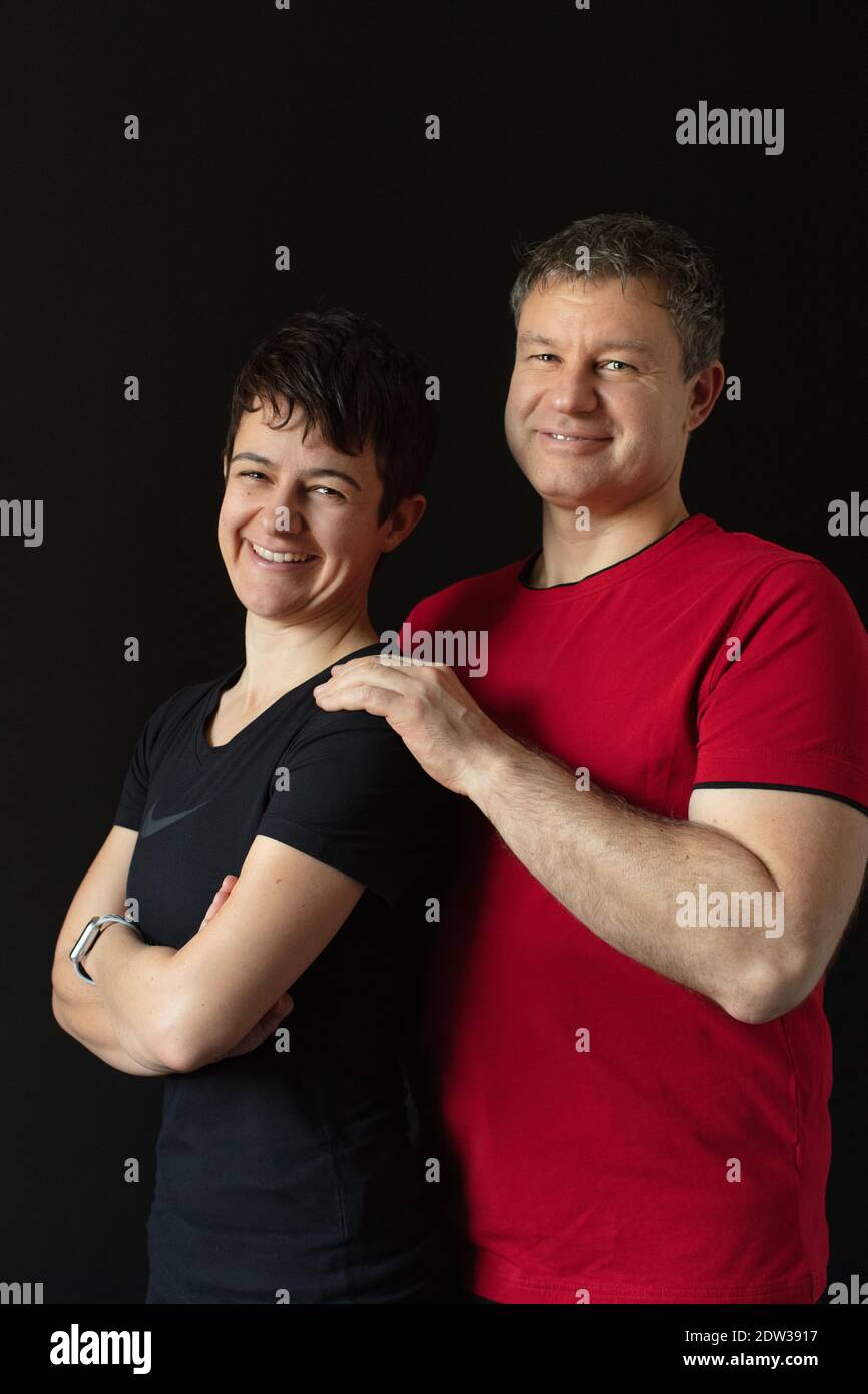 Caucasian athletic personal trainer couple dressed in red and in black posing back on back with crossed arms in front of a black background. Stock Photo