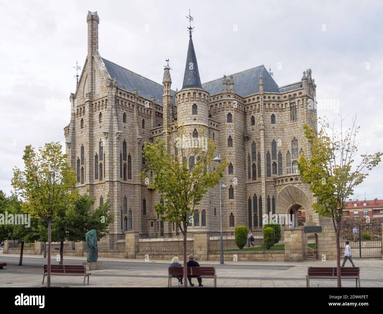 A couple is sitting on the bench in front of the Episcopal Palace of the Spanish architect Antoni Gaudi - Astorga, Castile and Leon, Spain Stock Photo