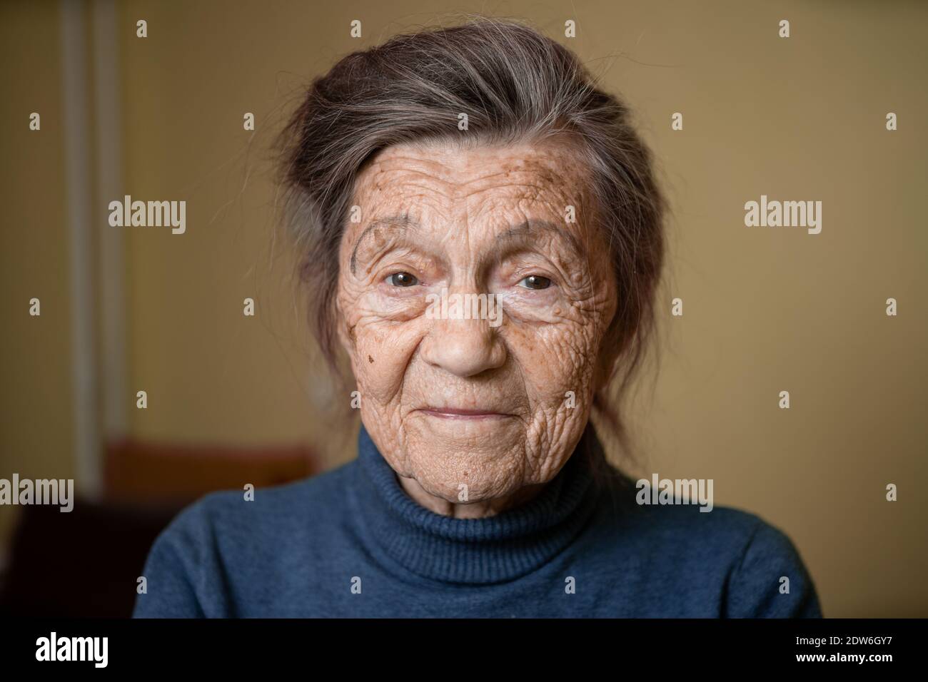 Elderly Caucasian senior grandmother ninety years old looks attentively and smiles, feels happy, large portrait, face with deep wrinkles, gray hair. T Stock Photo
