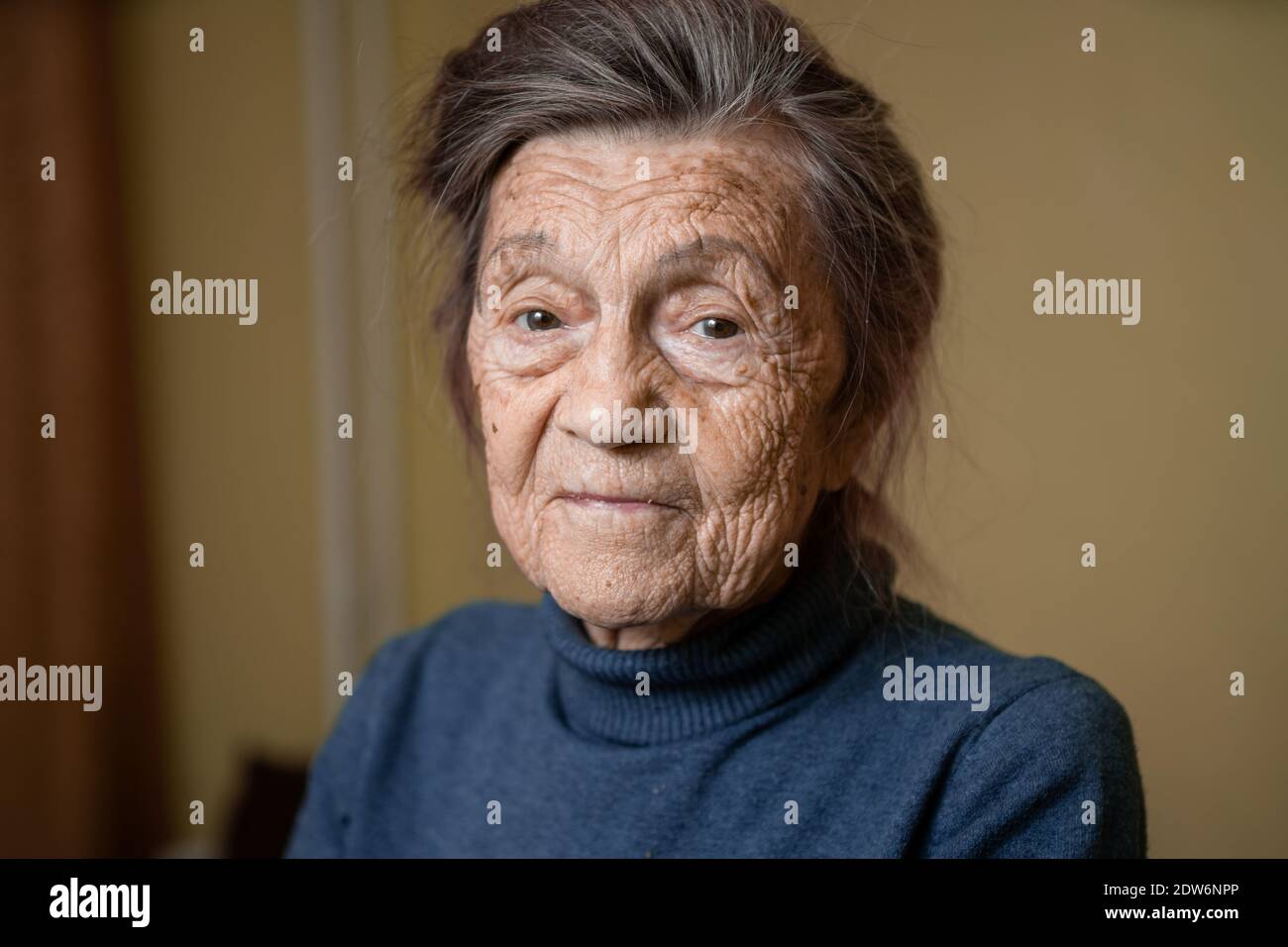 Elderly Caucasian senior grandmother ninety years old looks attentively and smiles, feels happy, large portrait, face with deep wrinkles, gray hair. T Stock Photo