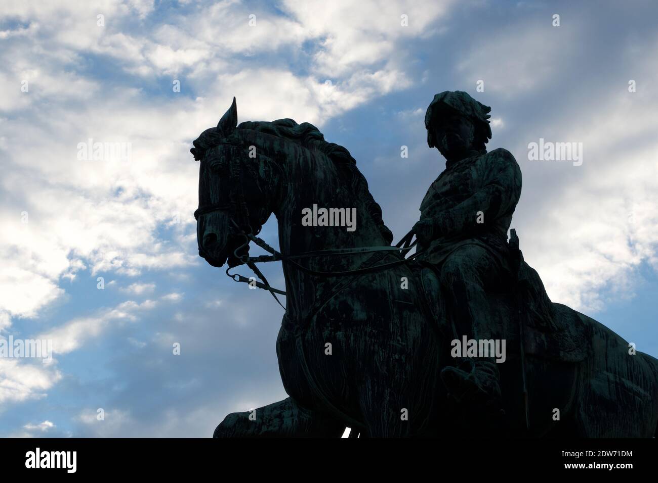 Silhouette of a dark metal statue of a soldier on a horse, standing boldly against a blue, cloudy sky. Stock Photo