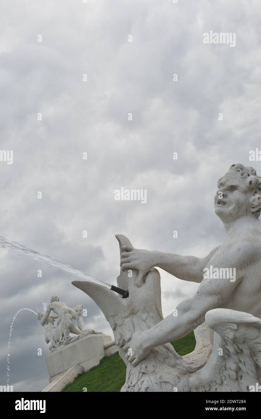 A white stone statue of an angry man holding open the beak of a bird; it is a fountain, and the bird is squirting water from its beak Stock Photo