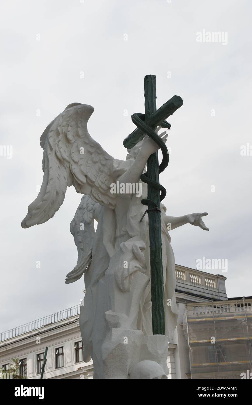 Statue of a white stone angel holding a dark cross with a serpent or snake, on a grey day Stock Photo