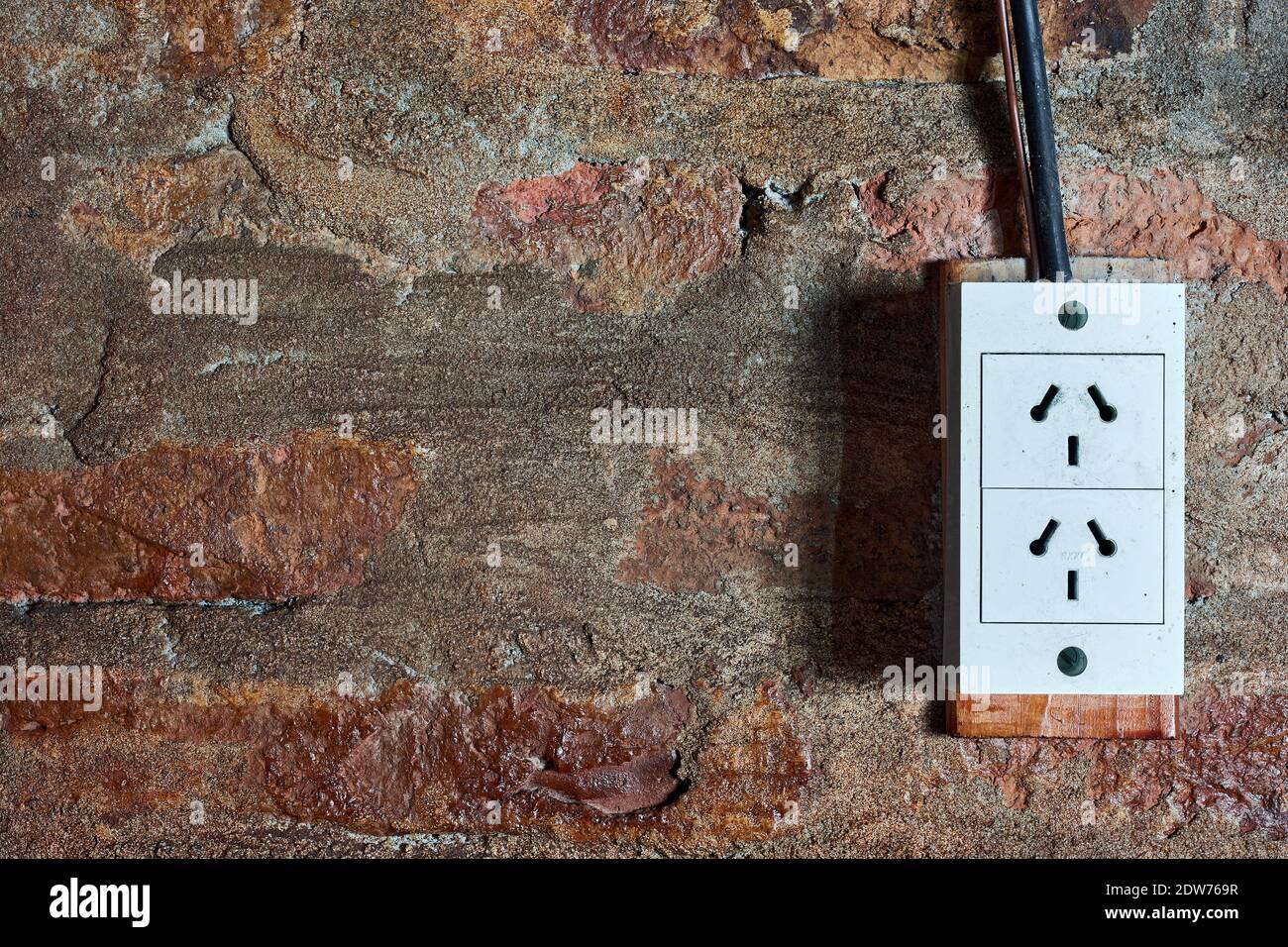 Old plug on background of red brick wall with grunge texture. Stock Photo