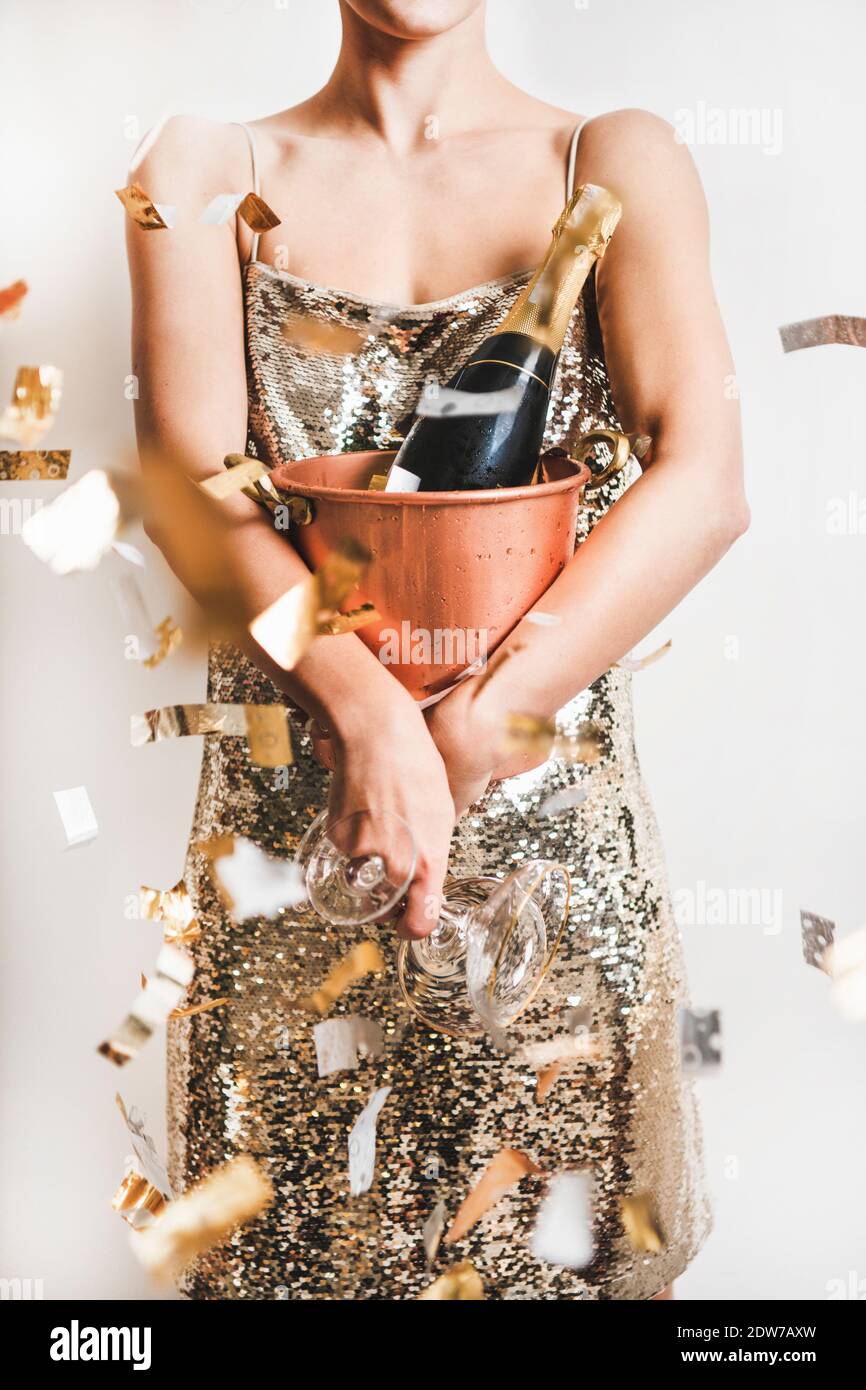 Young woman figure in festive glittering cocktail golden mini dress holding copper bucket with ice for champagne bottle and glasses over white wall wi Stock Photo