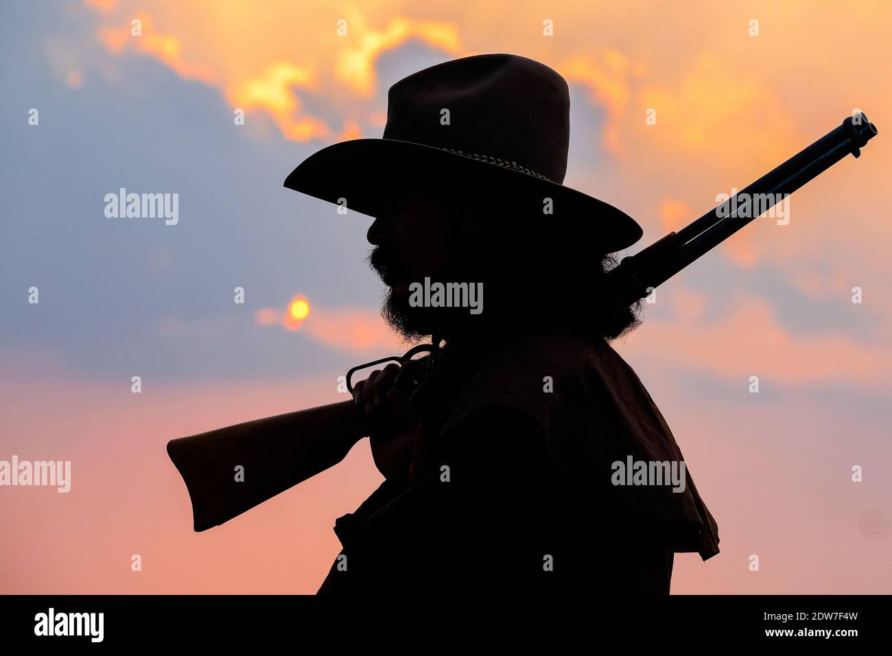 Side View Of Silhouette Man Holding Gun Against Sky During Sunset Stock Photo