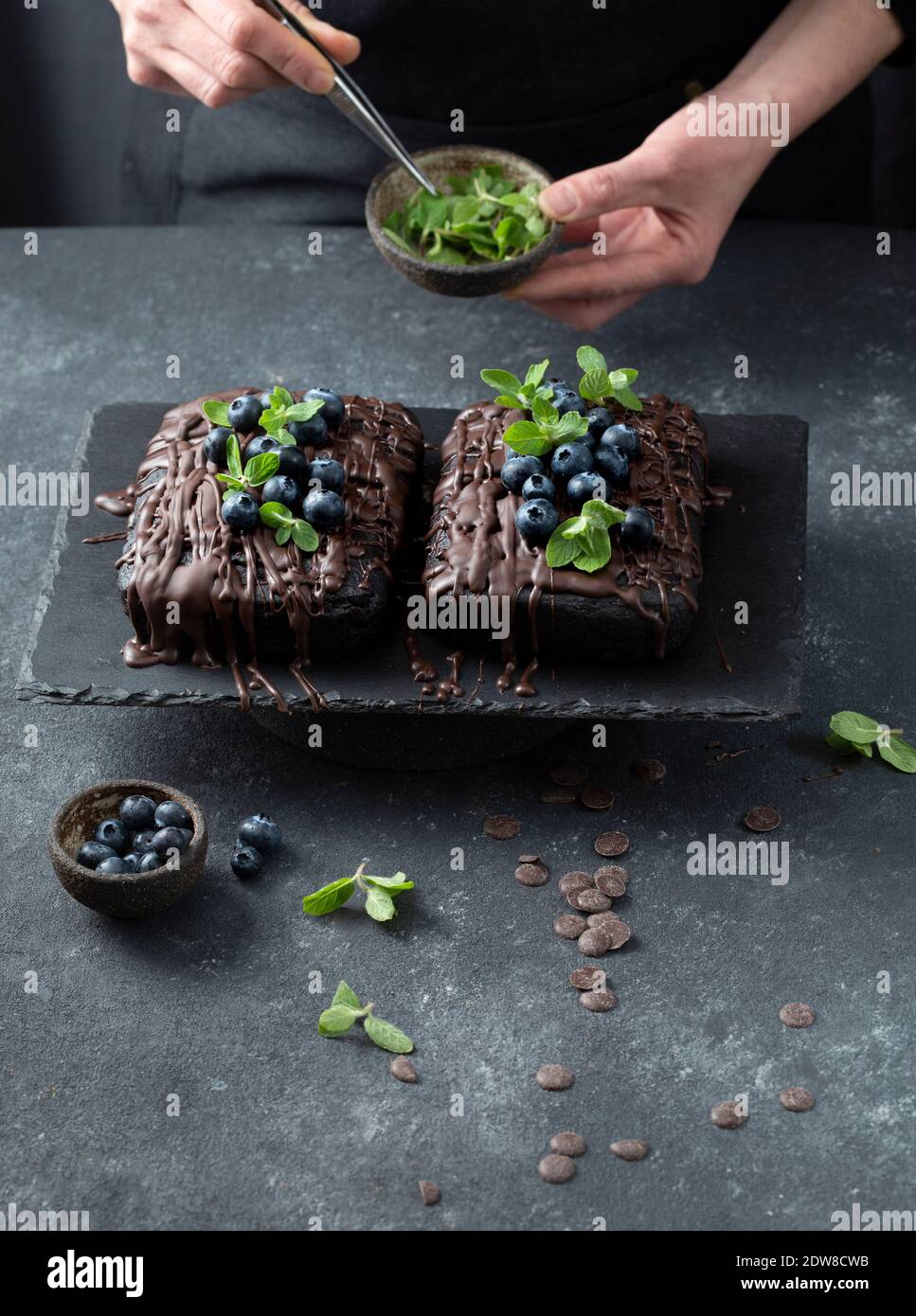 Pastry chef decorates brownie cake with blueberries and mint leaves. Stock Photo