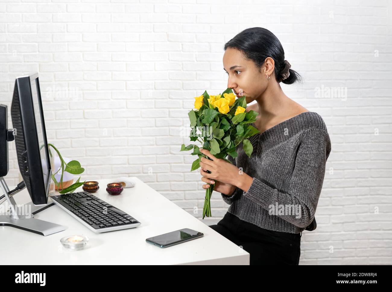 Young pretty woman holds a bunch of yellow roses in front of her face and speaking online Stock Photo